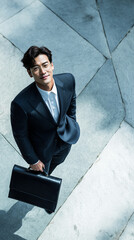 Fototapeta premium Confident young businessman in suit with briefcase looking up outdoors