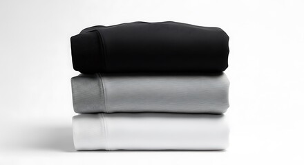 A neat stack of three folded t-shirts in black, grey, and white on a plain background.