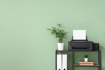 Stylish shelving unit with modern printer, houseplants and decor near green wall