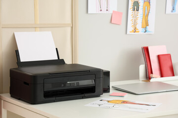 Workplace of clothes stylist with modern printer and laptop in light home office, closeup