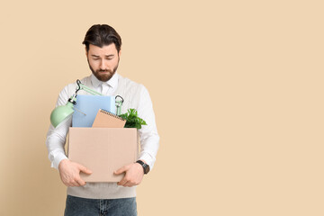 Fototapeta na wymiar Fired young man holding box with personal stuff on beige background