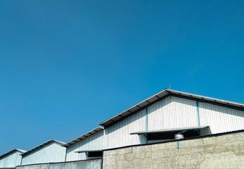 A row of industrial warehouse buildings with metal roofs, captured on a clear sunny day. Suitable for themes of logistics, storage, factory, or industrial zones.