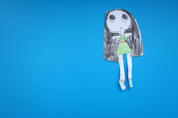 A children's paper doll, cut out and painted by hand, lies on a rich blue background.