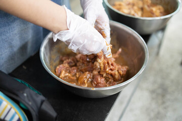 A person is cooking meat in a bowl with gloves on. The person is wearing a blue apron
