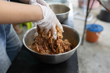 A person is cooking meat in a bowl with gloves on. The person is wearing a blue apron
