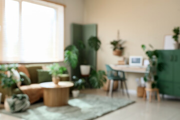 Blurred view of stylish office with comfortable workspace, cabinet, modern laptop and houseplants