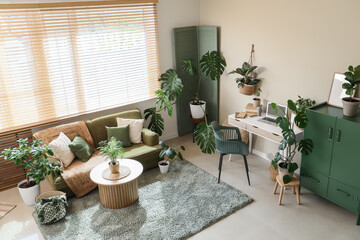 Interior of light office with comfortable workspace, cabinet, modern laptop and houseplants