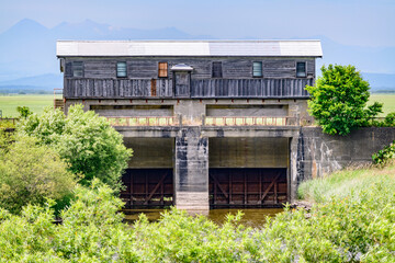 北海道釧路市にある旧岩保木水門を、7月の晴れた日に撮影。青空と緑に囲まれた歴史的建造物が、夏の澄んだ空気の中に佇む。