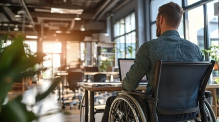 A man in a wheelchair working on a laptop in an office.