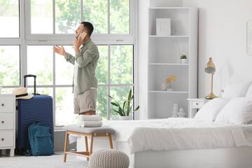 Male tourist talking by mobile phone near window in hotel room