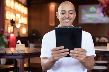 Confident Bald Hispanic man in white polo shirt sitting in Chinese style coffee shop
