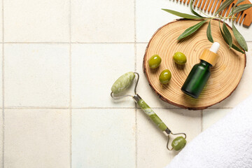 Composition with bottle of essential oil, facial massage tool, hair comb and green olives on light tile background