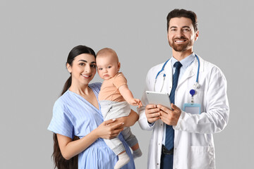Fototapeta premium Mother with her little baby and pediatrician on grey background