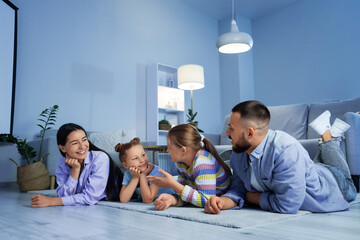 Fototapeta premium Happy parents with their daughters watching cartoons at home in evening