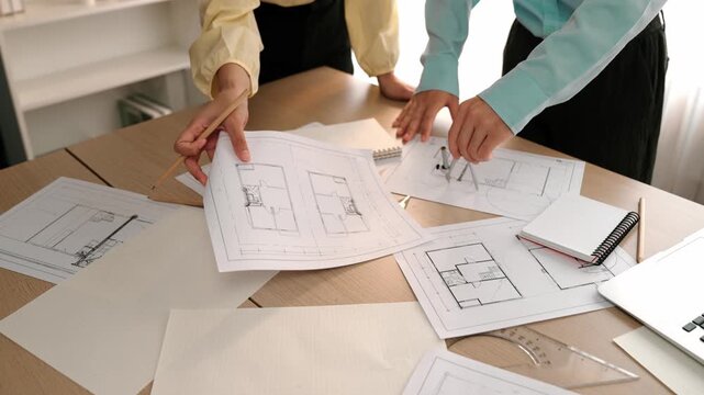 Architect and safety engineer discussion about building blueprint displaying on laptop on table with architectural document and wooden block scatter around at modern office. Closeup. Delineation.