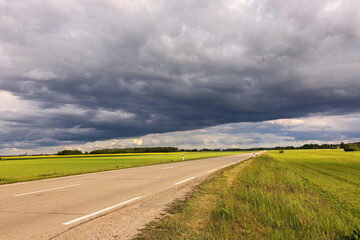 Cloudy sky over a country road surrounded by green fields and distant trees