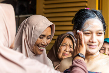 Indonesian women applying makeup on pregnant woman during mitoni ceremony