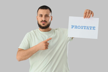 Young man pointing at paper with word PROSTATE on light background. Cancer awareness concept