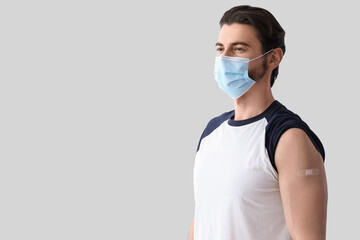 Young man in medical mask with applied patch after vaccination on light background