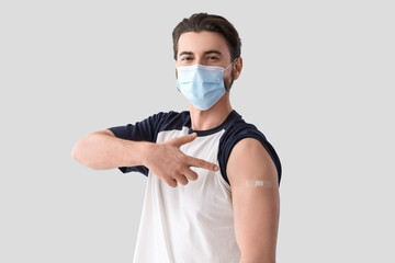 Young man in medical mask pointing at applied patch after vaccination on light background