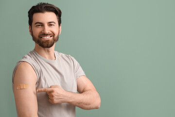 Young man pointing at applied medical patch after vaccination on green background