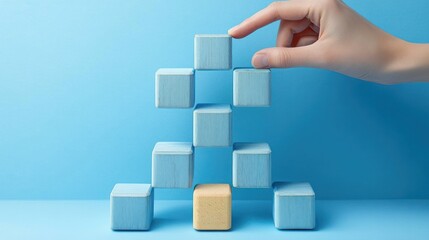 Hand carefully placing a light blue wooden block on top of a stepped pyramid structure of wooden blocks on a blue background, symbolizing growth and balance