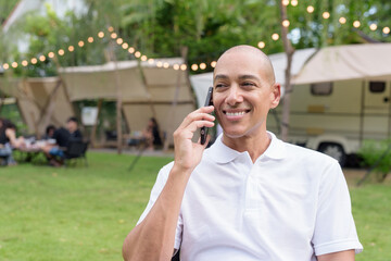 Confident bald man relaxing at campsite with camper van using phone