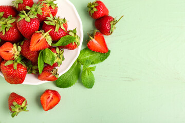 Plate with sweet ripe strawberries and mint leaves on green wooden background © Pixel-Shot