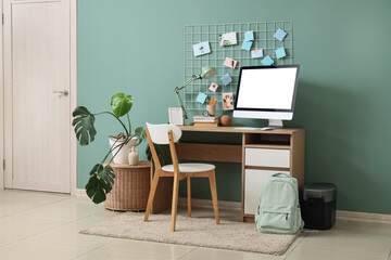 Comfortable workspace with modern computer, portable power station and mood board near blue wall