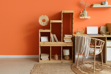 Obraz premium Comfortable workspace with modern laptop and shelving unit near orange wall