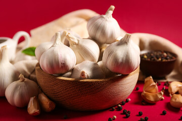 Wooden bowl with fresh garlics and peppercorns on red background
