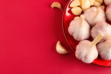 Plate with fresh garlics on red background