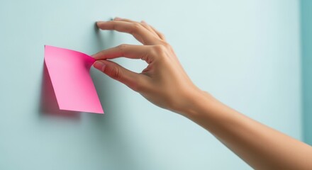 Hand placing a pink sticky note on a light blue wall