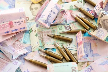 Many rifle bullets lies on lots of ukrainian money bills close up
