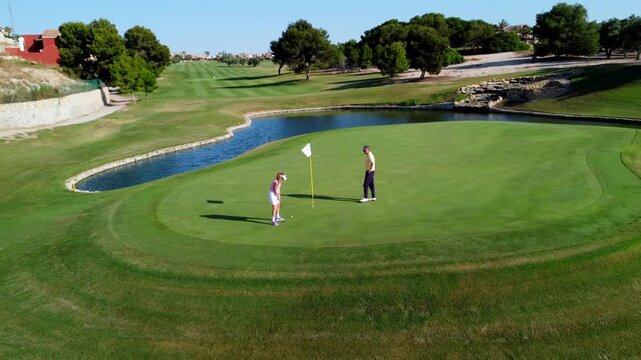 Golf instructor assisting female golfer on putting green