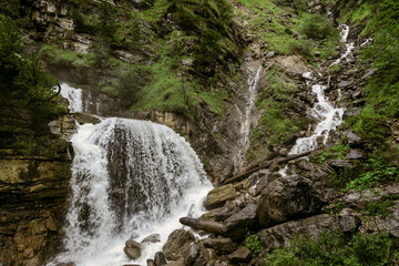 Stunning view of the multi-tiered Kuhflucht Gorge waterfall in Farchant, Bavaria, Germany. The cascading water flows down steep rock formations surrounded by lush green forest, showcasing the natural 