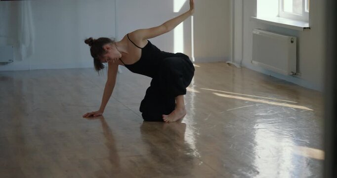Girl in black suit performs smooth movement during her contemporary parter choreography on the floor in choreography studio. Slow and graceful dance movement