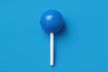 A solitary blue lollipop stands out against a vibrant blue backdrop, symbolizing sweetness and simplicity