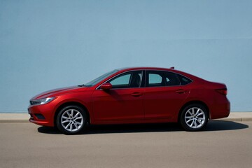 Naklejka premium A vibrant red sedan stands out against a serene blue sky, its sleek design reflecting modern automotive elegance