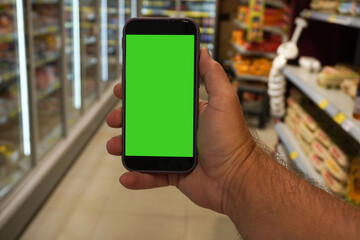 Customer holding smartphone with green screen in supermarket