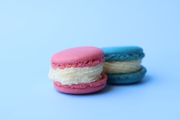 Colorful pink macaron with generous cream fillings on a blue background. Traditional dessert cookie.