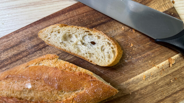 Crusty baguette slice on rustic board whispers simplicity of Sourbread Day, evoking French picnics, artisanal bread crafting