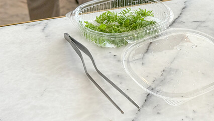 Elegant steel tongs beside fresh microgreens evoke gourmet rituals before Holi brunch, celebrating renewal with culinary zest
