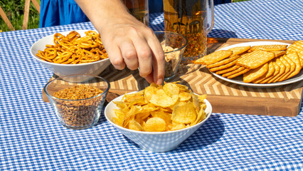 Hand reaching for crispy delight at a gingham-laden picnic, reminiscent of Oktoberfest's convivial camaraderie and National Chip Week indulgence