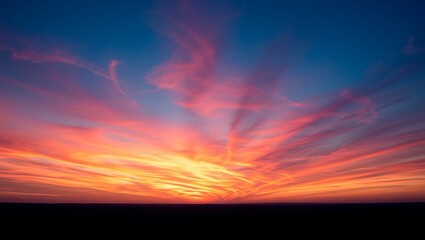 Obraz premium A vibrant sunset with pink and orange clouds radiating across the blue sky above a dark horizon line