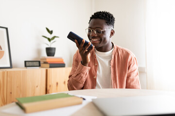Smiling young man using voice assistant on smartphone at home office