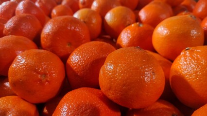 A close-up of fresh, vibrant oranges piled together, their bright skin glistening under the light, evoking a sense of freshness and natural sweetness.
