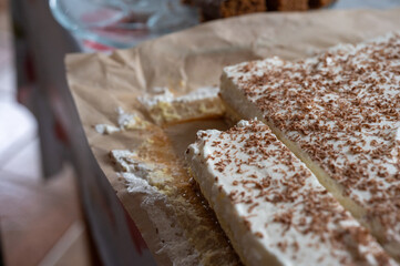 Close-up of a slice being removed from a homemade cake with whipped cream and grated chocolate topping, served on parchment paper.