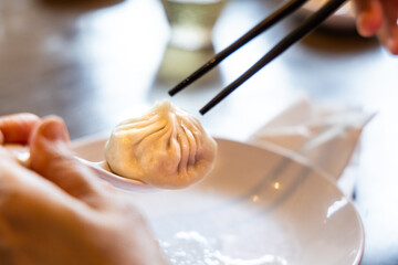 Diner picking up Shanghai popular xiaolongbao or little dragon dumpling with spoon and chopsticks at restaurant