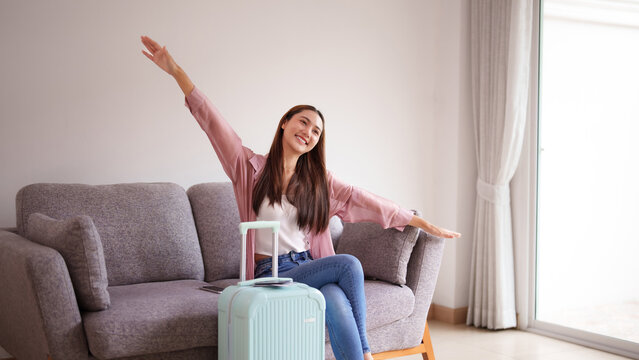 Asian adult woman happily prepares travel adventure plans journey home comfortable living room light suitcase vacation excitement